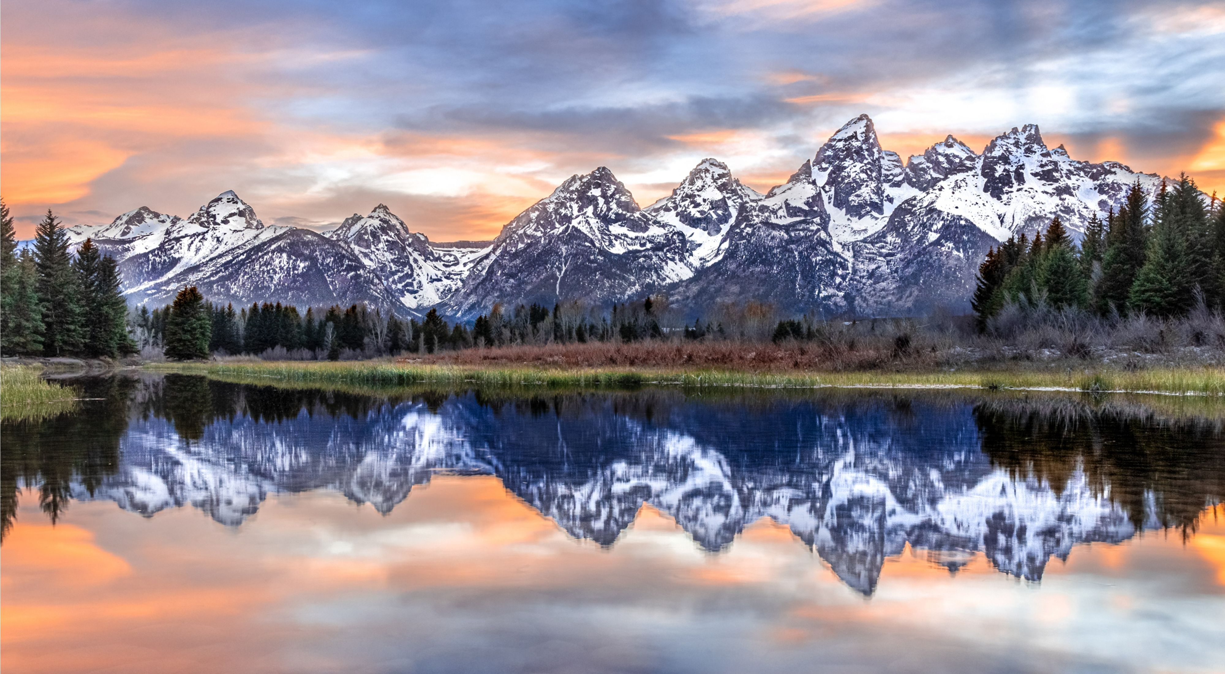 a snowy mountain range with a pond in the foreground. 